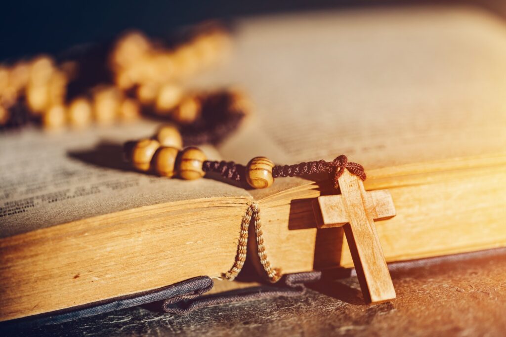 Rosary with cross laying on a Bible book.